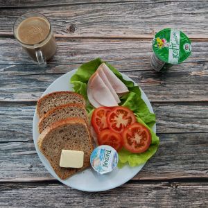 Zdjęcie przedstawia Dietę z ograniczeniem łatwoprzyswajalnych węglowodan&oacute;w: Chleb Graham Masło extra Kawa zbożowa z mlekiem Serek twarogowy termizowany smak śmietankowy Kefir Pomidor Szynkowa dębowa drobiowa kiełbasa grubo rozdrobniona Sałata zielona